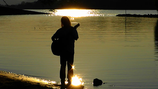 person playing guitar infront of body of water during daytime thumbnail