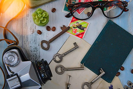 Four Gray Skeleton Keys Next to Gray Camera, Black Book, and Brown Framed Eyeglasses thumbnail