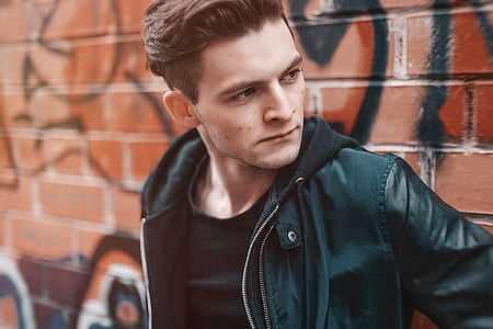 man leaning on brown brick wall with graffiti thumbnail