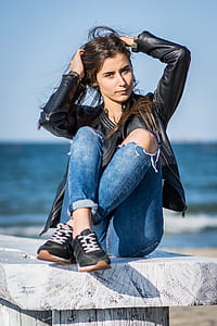 woman wearing black jacket sitting on bench holding her hair during day thumbnail