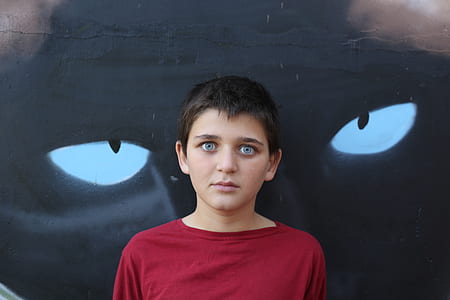 boy with blue eyes wearing red crew-neck shirt leaning on wall with eyes painting thumbnail