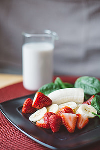sliced banana and strawberry on plate beside glass of milk thumbnail