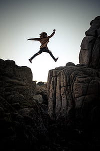 woman jumping from rock to rock during daytime thumbnail