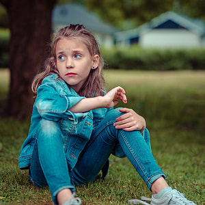 girl wearing denim jacket and denim jeans sitting on bed of green grasses thumbnail
