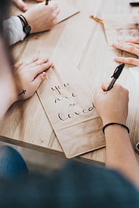 person writing on brown paper with you are so loved using black ballpoint pen thumbnail