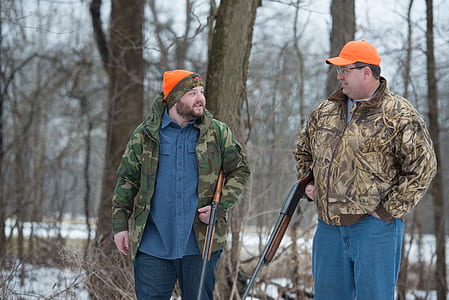two male hunters holding hunting rifles walking in the woods thumbnail