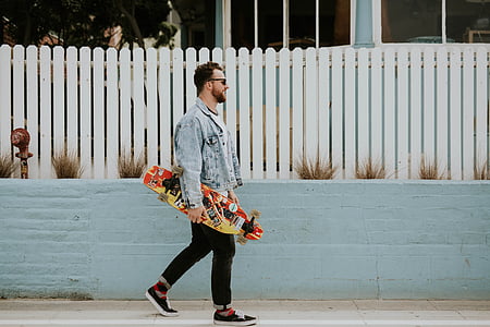 man walking near fence carrying skateboard thumbnail