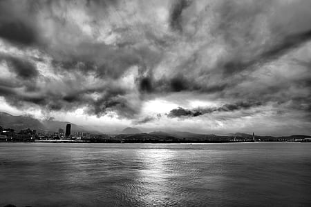 Grayscale Photo of Calm Body of Water Under Cloudy Sky thumbnail
