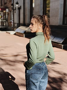 woman in green shirt and blue jeans standing near building thumbnail
