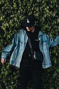 man wearing blue denim button-up jacket and black LA cap near leafed wall plant thumbnail