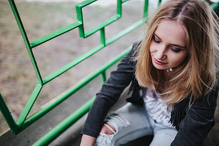 Blonde woman in a black jacket and ripped jeans by a green handrail thumbnail