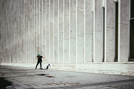 A young caucasian skateboarder wearing cap rides past a city building thumbnail