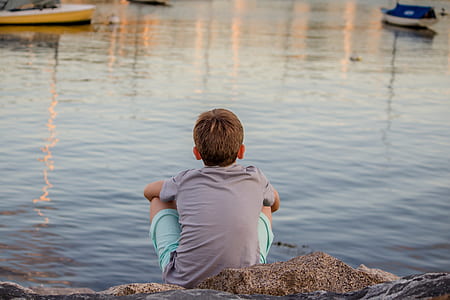 boy sitting in front of body of water during daytime thumbnail