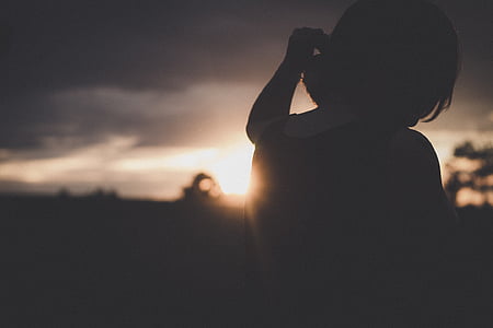 silhouette photography of woman raising her left hand under dark sky thumbnail