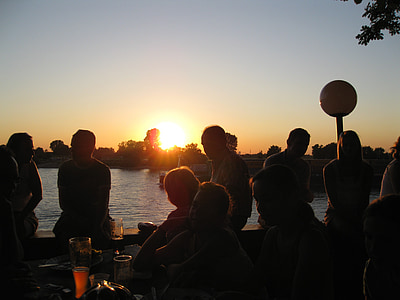 silhouette photo of people sitting beside body of water during golden hour thumbnail