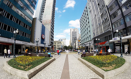 people walking at the parked in between two high-rise glass buildings under white clouds and blue sky thumbnail