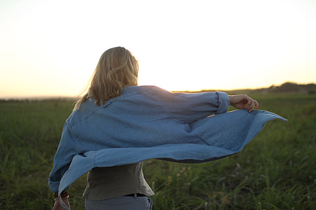 woman wearing blue denim long sleeve shirt and white pants while standing top of green grass under white sky thumbnail