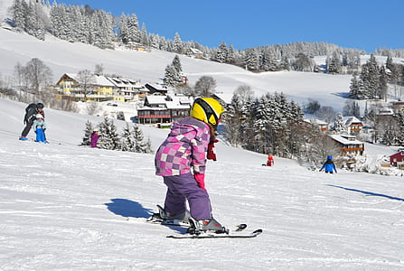 girl wearing skis near people and houses at the field during winter thumbnail