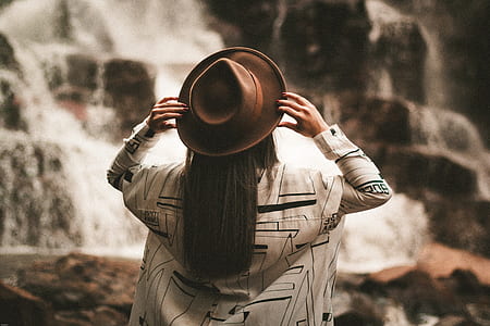 woman holding brown fedora hat looking at waterfalls thumbnail