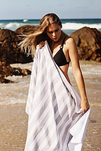 woman standing on seashore while holding towel thumbnail