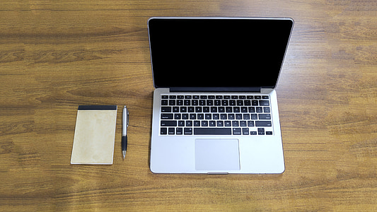 MacBook Pro, white pad, and silver click pen on top of brown wooden table thumbnail