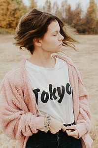 selective focus photography of women's white Tokyo-print mesh crew-neck shirt and pink fleece cardigan standing on grass field at daytime thumbnail