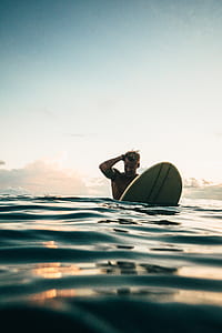 man riding surfboard on body of water againsts gray and blue sky thumbnail