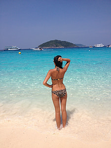 woman standing on seashore overlooking the boat and island during daytime thumbnail