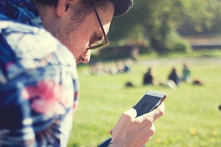 tilt shift photo of a man holding smartphone in the park thumbnail