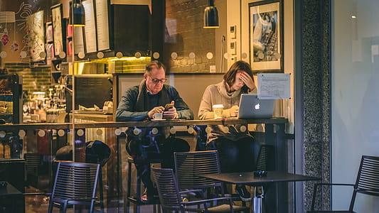 man wearing grey coat sitting on chair beside woman while using MacBook thumbnail