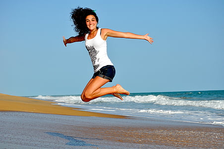 woman wearing white tank top jumping near seashore thumbnail