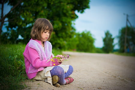 girl wearing pink coat and purple leggings sitting on ground during daytime thumbnail