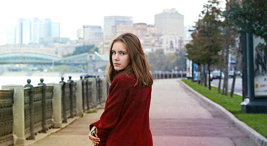 woman in red jacket on gray concrete road near body of water during daytime thumbnail