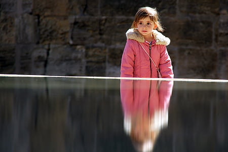 girl wearing white and pink fleece collared topcoat standing near body of water thumbnail