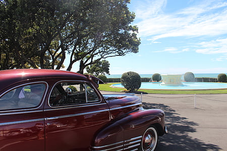 classic red vehicle near tree and water fountain at daytime thumbnail