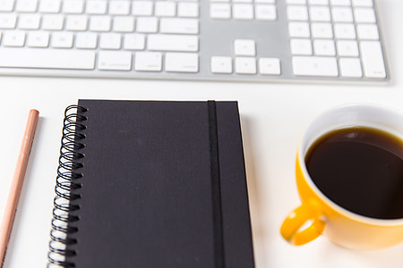 Computer keyboard, coffee cup, notebook and pencil on a white desk thumbnail
