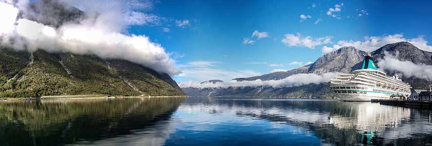 white crew ship on body of water beside green and gray mountains thumbnail