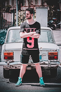 Man Wearing Black Scoop-neck T-shirt and Black Gym Shorts Standing Behind White Vehicle thumbnail