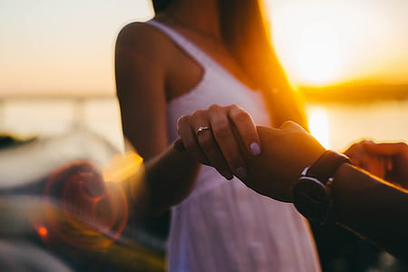woman holding person's left hand closeup photo with view of body of water during golden hour thumbnail