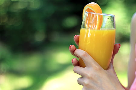 Glass of orange juice in the hands of woman in nature thumbnail
