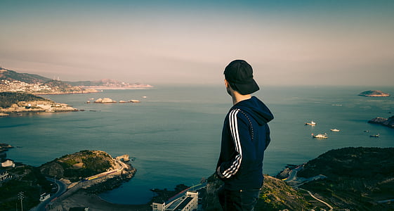 man on mountain overlooking body of water and buildings thumbnail