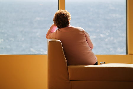 woman sitting on couch facing window pane with view of body of water thumbnail