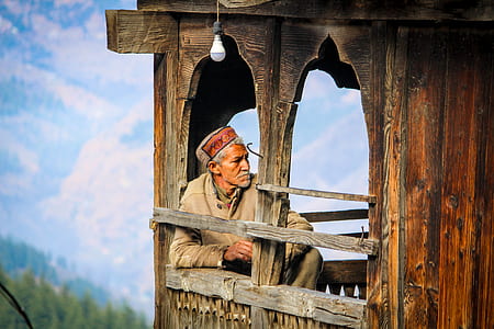 man sitting on brown wooden chair near window thumbnail