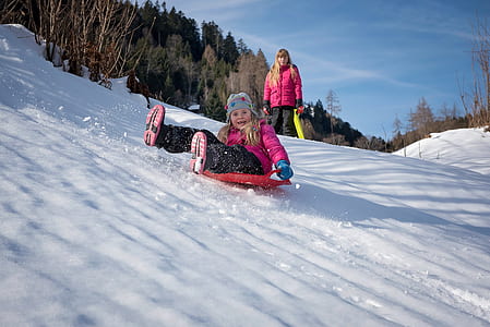 girl riding red plate playing on snow thumbnail