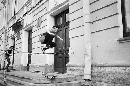 Grayscale Photography of Man Riding Skateboard Making Tricks Near Concrete Building thumbnail