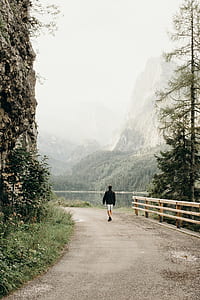 man walking on ground between river and rock near mountain range thumbnail
