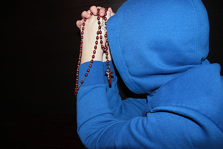 person wearing blue pullover hoodie praying with rosary thumbnail