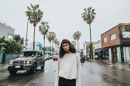 man wearing white sweatshirt standing on black concrete road near grey vehicle thumbnail
