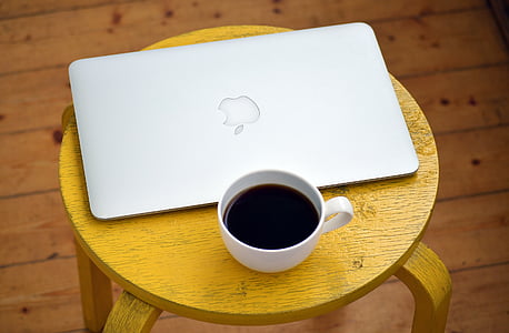 black coffee filled white cup and MacBook Air on top of brown wooden table thumbnail
