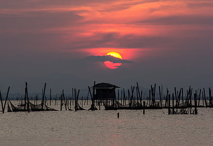 silhouette of house on body of water at golden hour thumbnail